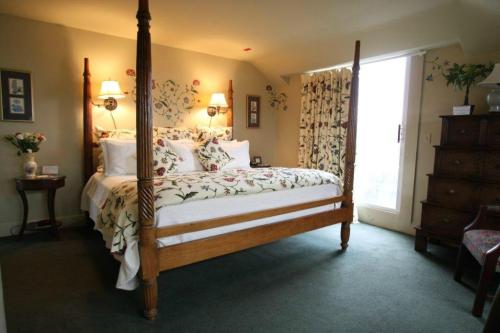 Cozy bedroom with a four-poster bed, floral bedding, and soft lighting, featuring a window and decorative curtains.