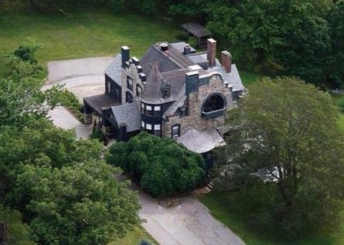 Aerial view of a large, dark stone mansion surrounded by trees and a winding driveway.