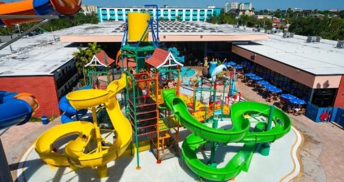 A colorful water park featuring multiple slides and play structures, surrounded by a pool and dining area.