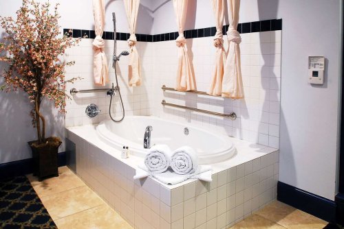 A spacious bathroom featuring a white tub, pink curtains, and neatly arranged towels on the edge.