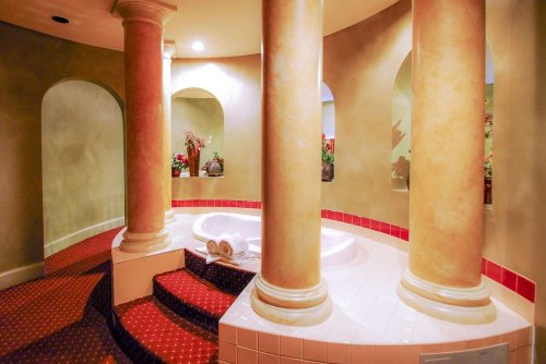 A luxurious spa area featuring a hot tub, decorative columns, and plush red carpeting.