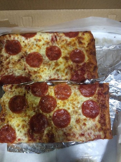 A rectangular pizza with pepperoni slices on top, partially in a pizza box lined with foil.