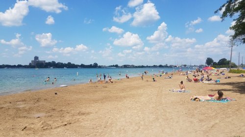 A sandy beach with people sunbathing and swimming, under a blue sky with fluffy clouds and a calm water view.