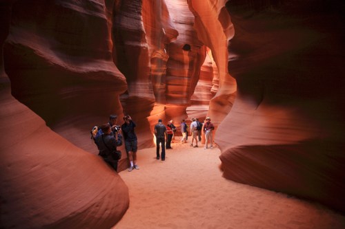 Visitors explore the narrow, winding passage of Antelope Canyon, surrounded by stunning red rock formations.