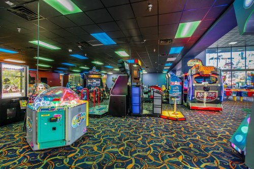 Brightly lit arcade with various gaming machines and colorful decor, featuring claw machines and racing games.