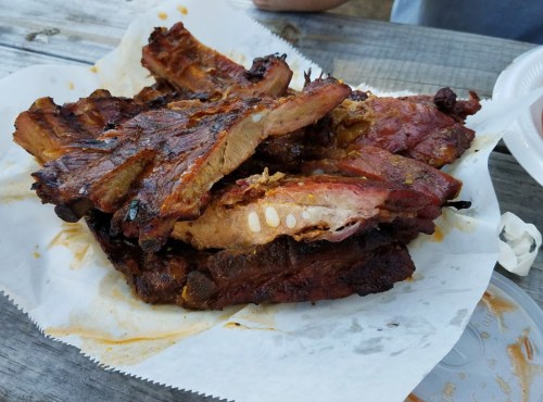 A pile of grilled ribs on a paper plate, showcasing a smoky, charred exterior and juicy meat.