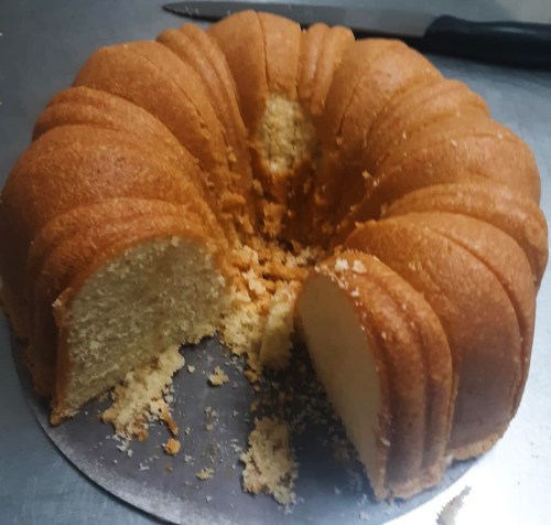 A freshly baked bundt cake with a slice cut out, resting on a silver cake board. Crumbs scattered around.