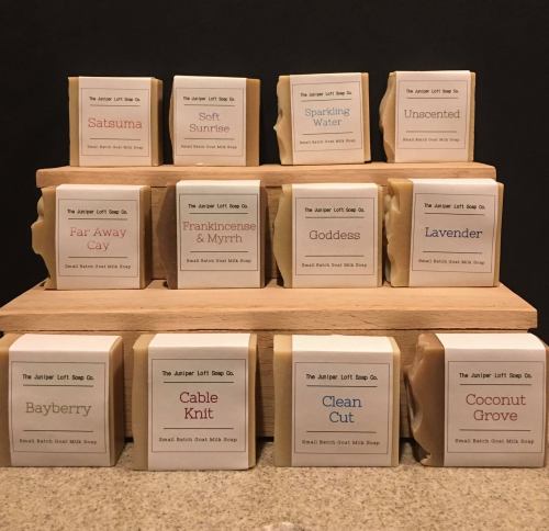 A display of assorted handmade soap bars in various scents, arranged on a wooden stand.