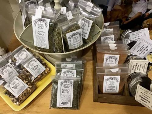A variety of spice packets displayed in a metal container and on a wooden surface, labeled with names and prices.