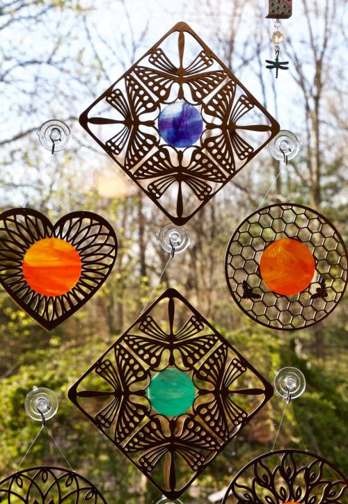 Colorful stained glass window hangings in various shapes, including hearts and diamonds, with a natural background.