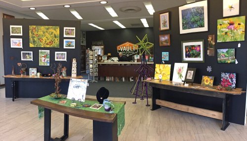 Art gallery interior featuring colorful paintings, sculptures, and a reception area with a staff member at the counter.