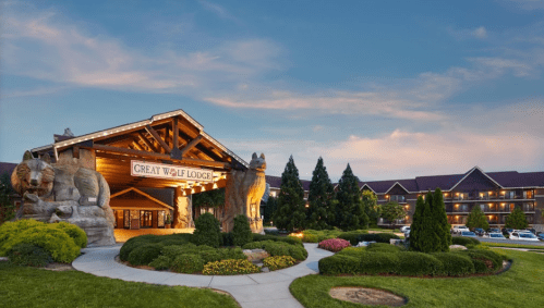 Exterior view of Great Wolf Lodge featuring wooden wolf sculptures and landscaped gardens under a blue sky.