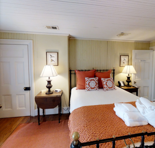 Cozy bedroom with a double bed, orange accents, two lamps, and a warm, inviting atmosphere.