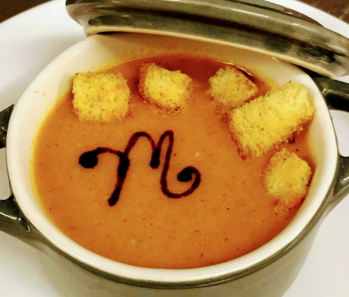 A bowl of soup topped with croutons and a decorative swirl, served in a small pot.