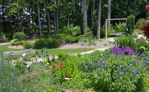 A vibrant garden filled with colorful flowers, greenery, and a winding path, surrounded by tall trees and a gazebo.