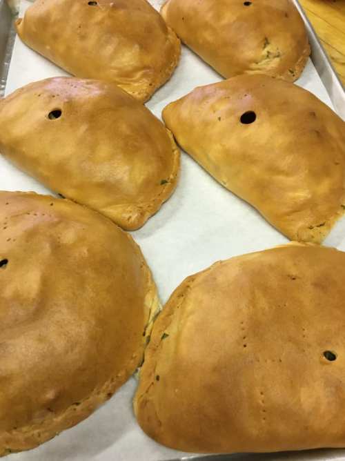 A tray of golden-brown calzones with a small hole on top, resting on parchment paper.