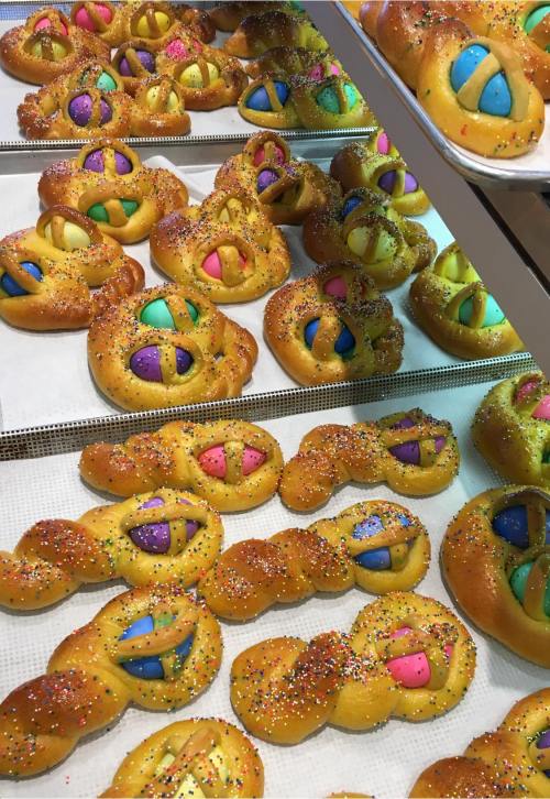 Colorful pastries shaped like bunnies, decorated with vibrant icing and sprinkles, arranged on a display tray.
