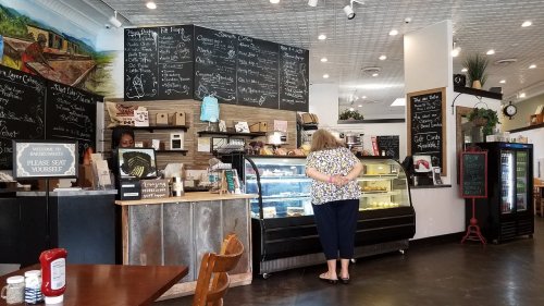 A cozy café interior with a chalkboard menu, a display case of desserts, and a customer browsing the options.
