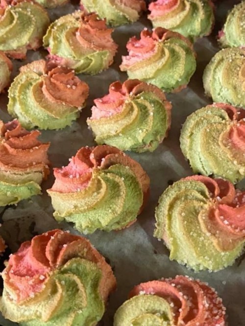 Colorful swirled cookies in shades of pink and green, sprinkled with sugar, arranged on a baking sheet.