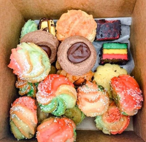 A box filled with colorful assorted cookies and small pastries, featuring swirls and layered treats.