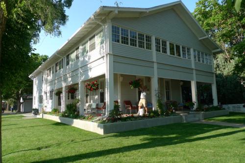 A large white house with flower boxes, surrounded by green grass and trees, with a person tending to the plants.