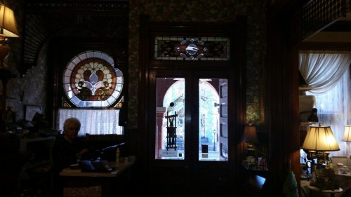 A cozy room with stained glass windows, vintage decor, and a woman sitting at a desk near the entrance.