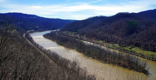 A winding river flows through a valley surrounded by mountains and bare trees under a clear blue sky.