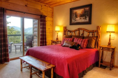Cozy bedroom with a wooden bed, red bedding, and a view of mountains through sliding glass doors.