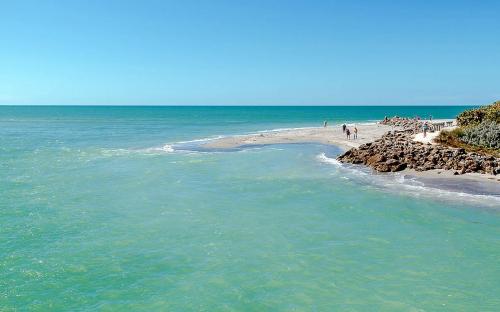 A serene beach scene with turquoise water, sandy shore, and people walking along the coast under a clear blue sky.