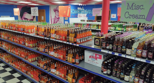 A colorful display of various soda bottles on shelves in a retro-themed store.