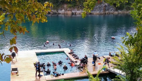 Divers prepare and explore in a serene lake, surrounded by trees and a wooden dock.