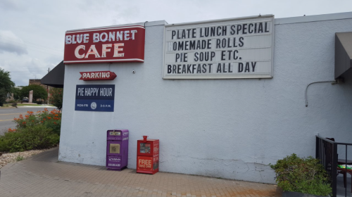 Signage outside Blue Bonnet Cafe advertising specials, including plate lunch, homemade rolls, and breakfast all day.