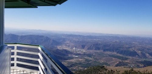A panoramic view from a balcony overlooking rolling hills and valleys under a clear blue sky.