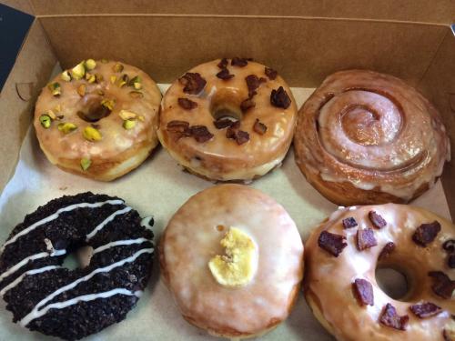 A box of assorted donuts, including glazed, chocolate, and topped with nuts and bacon.