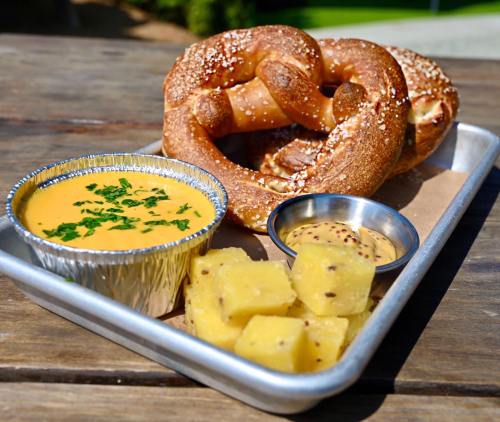 A tray with two pretzels, cheese dip, mustard, and diced pineapple.