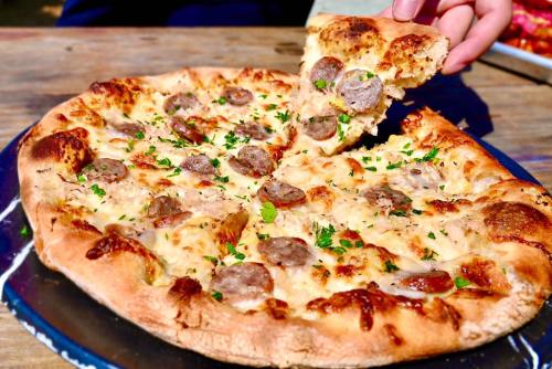 A freshly baked pizza topped with sausage slices and herbs, with a slice being lifted from the pie.