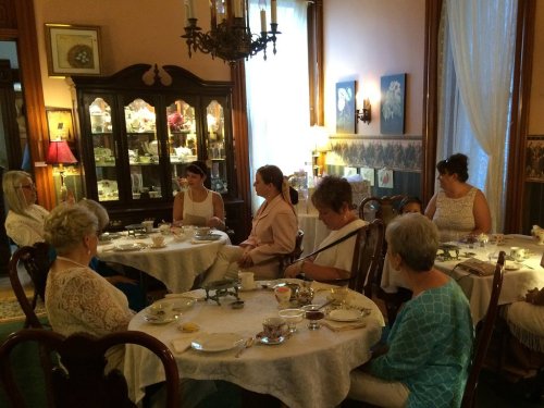 A group of women seated around a table in a vintage dining room, enjoying tea and conversation.