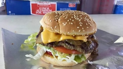 A sesame seed bun burger with lettuce, tomato, cheese, grilled onions, and a beef patty on a silver tray.