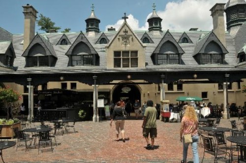 A historic building with a distinctive roof, featuring outdoor seating and people walking towards the entrance.