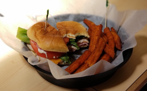 A sandwich with lettuce, tomato, and ham, served with sweet potato fries in a black basket.