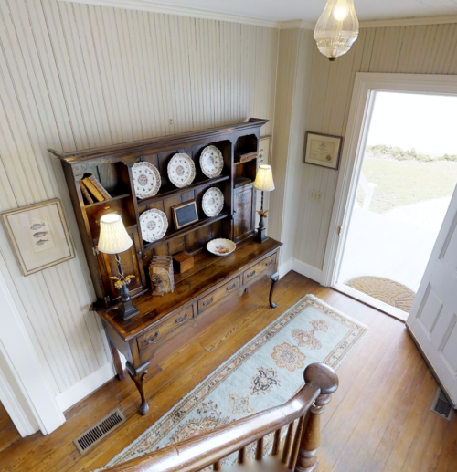 A wooden sideboard with decorative plates and lamps, set in a bright entryway with a view of the outdoors.
