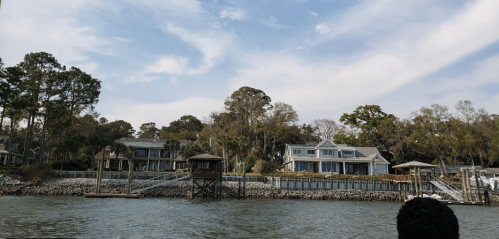Scenic view of waterfront homes with docks, surrounded by trees under a partly cloudy sky.