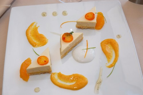 A plate with three triangular cheesecake slices, garnished with orange segments and drizzles of sauce.