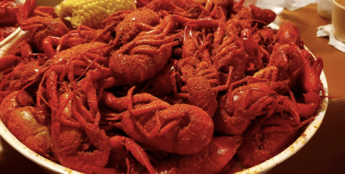 A large platter filled with spicy, red crawfish and a piece of corn on the side.