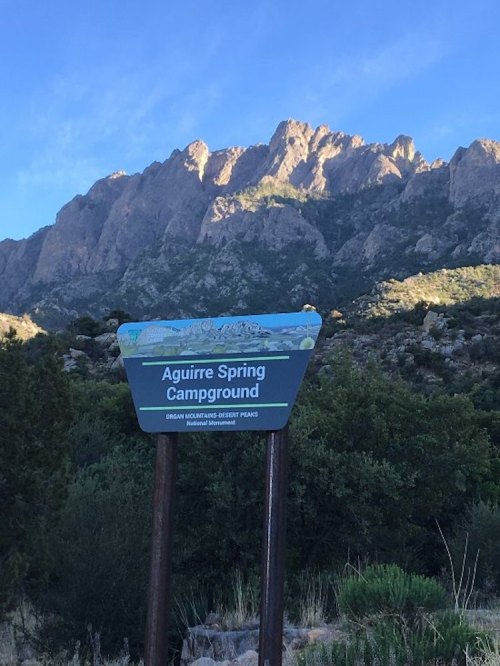 Sign for Aguirre Spring Campground with mountains in the background under a clear blue sky.