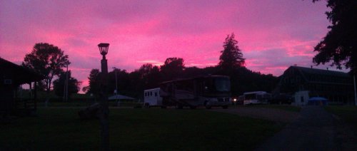 A vibrant pink sunset over a campground with RVs and trees silhouetted against the colorful sky.