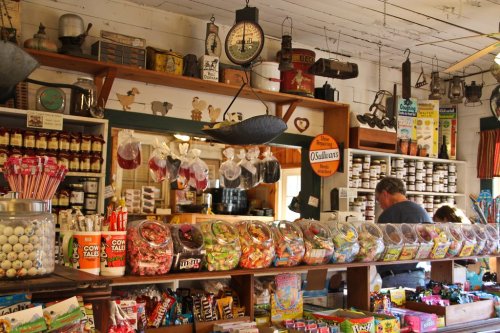 A colorful candy display in a vintage store, with jars of sweets and various products on shelves in the background.