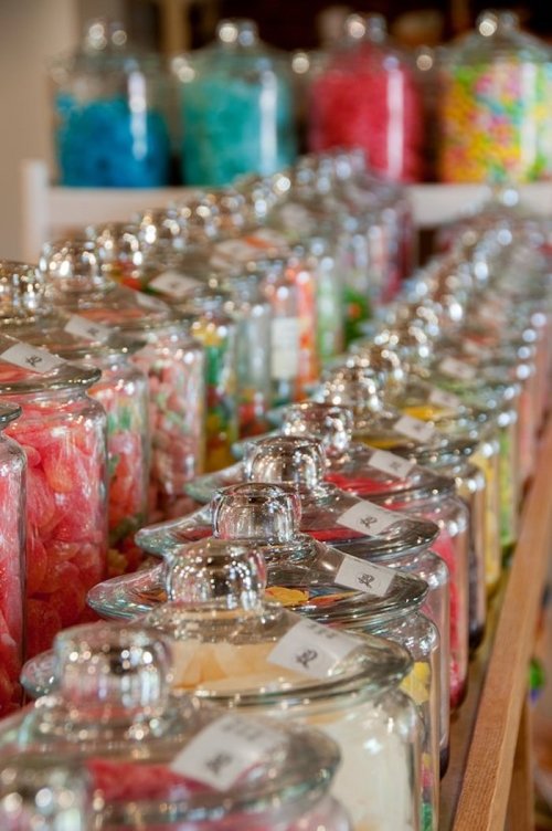 A colorful display of candy jars filled with various sweets, lined up on a wooden shelf.