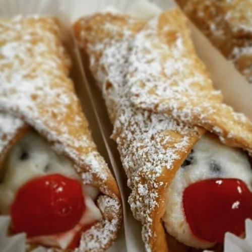 Close-up of cannoli filled with creamy filling, topped with a cherry and dusted with powdered sugar.