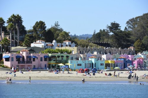Colorful beachside cottages line the shore, with people enjoying the sand and water on a sunny day.